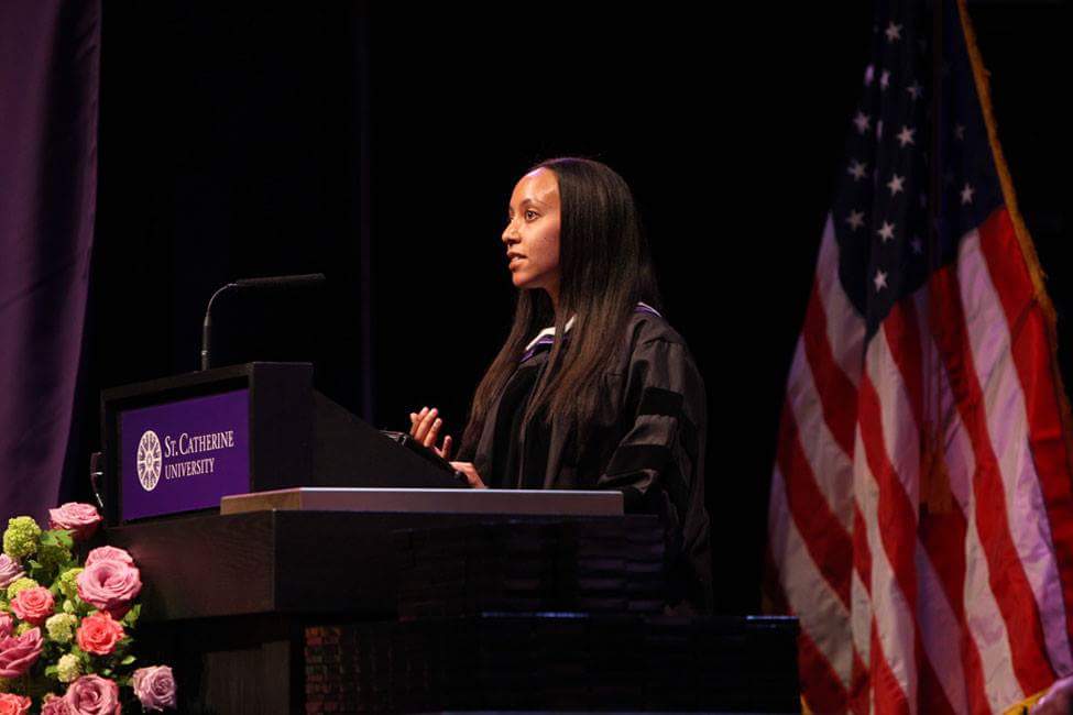 Video: Haben is standing at the St. Catherine University podium wearing academic regalia, and behind her is a US flag.