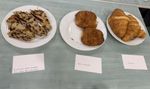 A line of plates full of delicious pastries sit on a table, and each one has a card with Braille and print. From left to right: Brioche with tonka bean and chocolate, Chocolate bread (Pain au chocolat), and croissant.