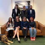 The group gathers together in the green room. Standing, from left to right: Troy Kotsur, Celimar Rivera Cosme, and Julian Ortiz. Sitting on the couch, from left to right: Haben Girma, Sarah Herrlinger, Bobbi Cordano, and Harmony Baniaga. Seeing Eye dog Mylo is on the floor beside Haben. On the back wall hangs a framed photo of Apple Park. Photograph provided by Apple.