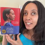 I'm smiling and holding up a book. The cover has a photo of me in profile, standing confidently in a blue dress. There is Japanese text along the side and bottom.