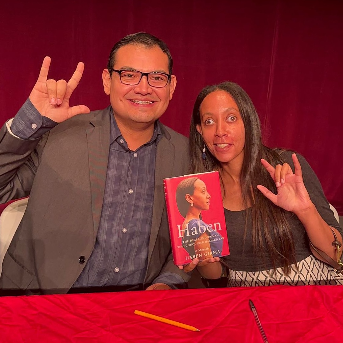 I’m sitting on stage with disability advocate and Deaf educator Yahir Alejandro. We’re signing ILY and holding up my book between us.
