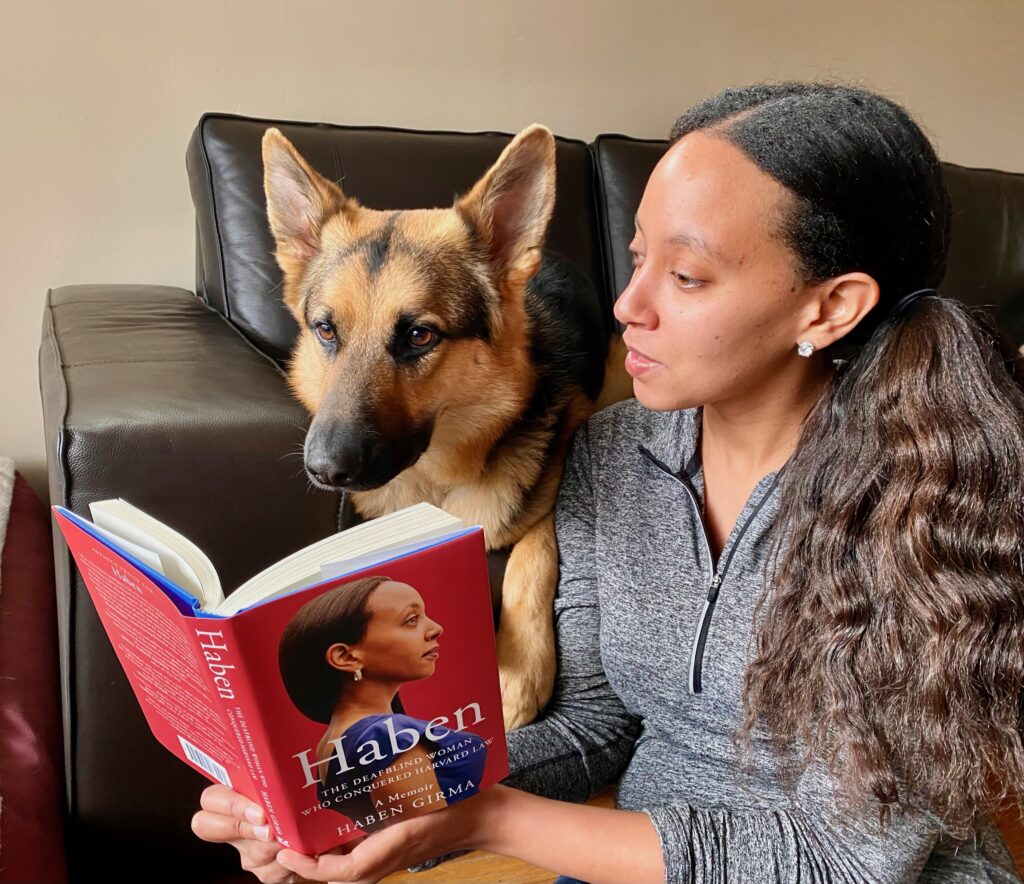 I’m sitting on the floor in front of a black sofa holding up my book for Mylo, my German Shepherd guide dog. He’s lying on the sofa looking down at the book. He will neither confirm nor deny that he read my memoir.‬